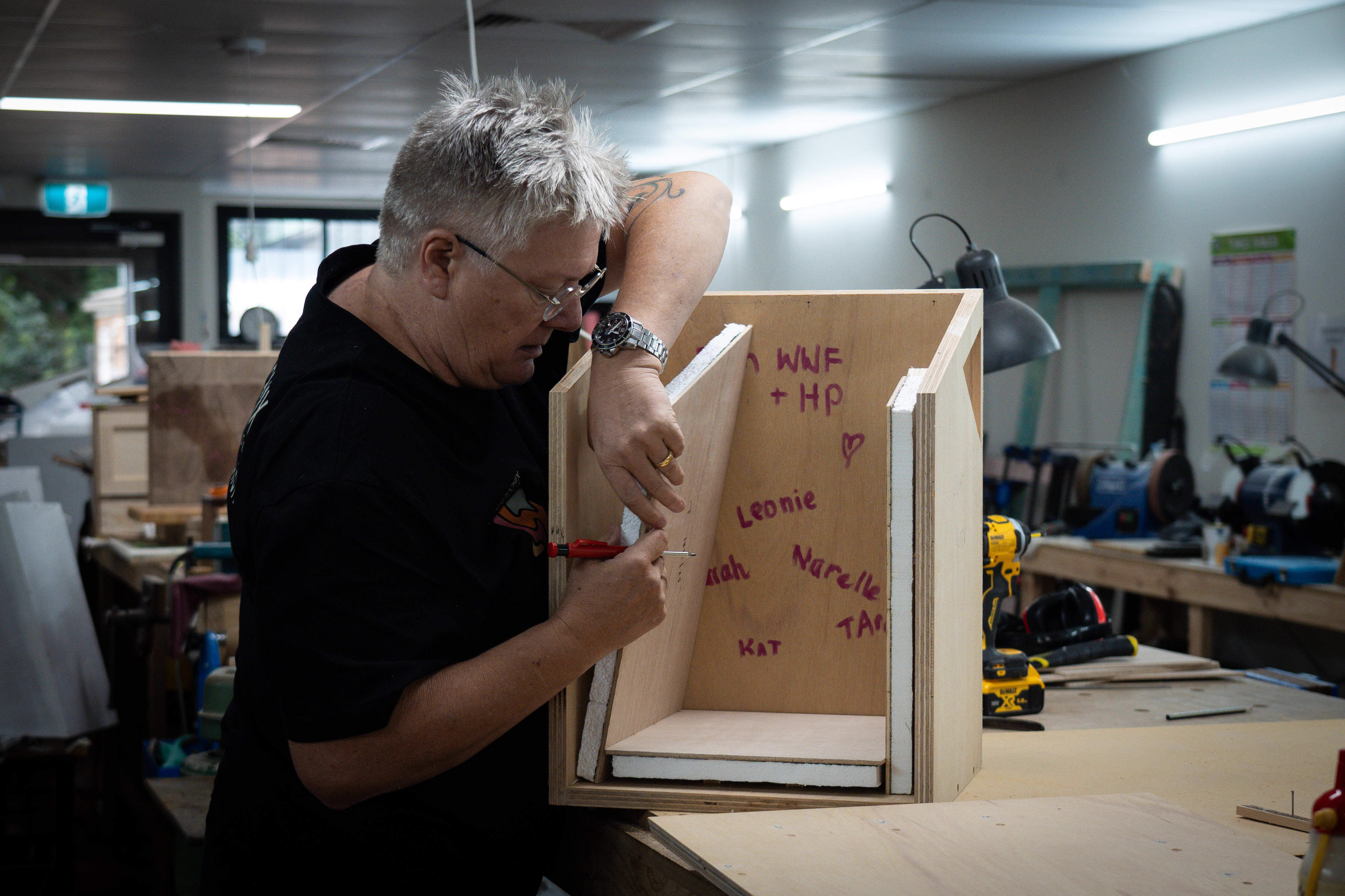 Founder of Woodchix Gill Enterkin constructs a nest box for greater gliders in a workshop environment. People have signed their names on the inside of the timber greater glider nest box.