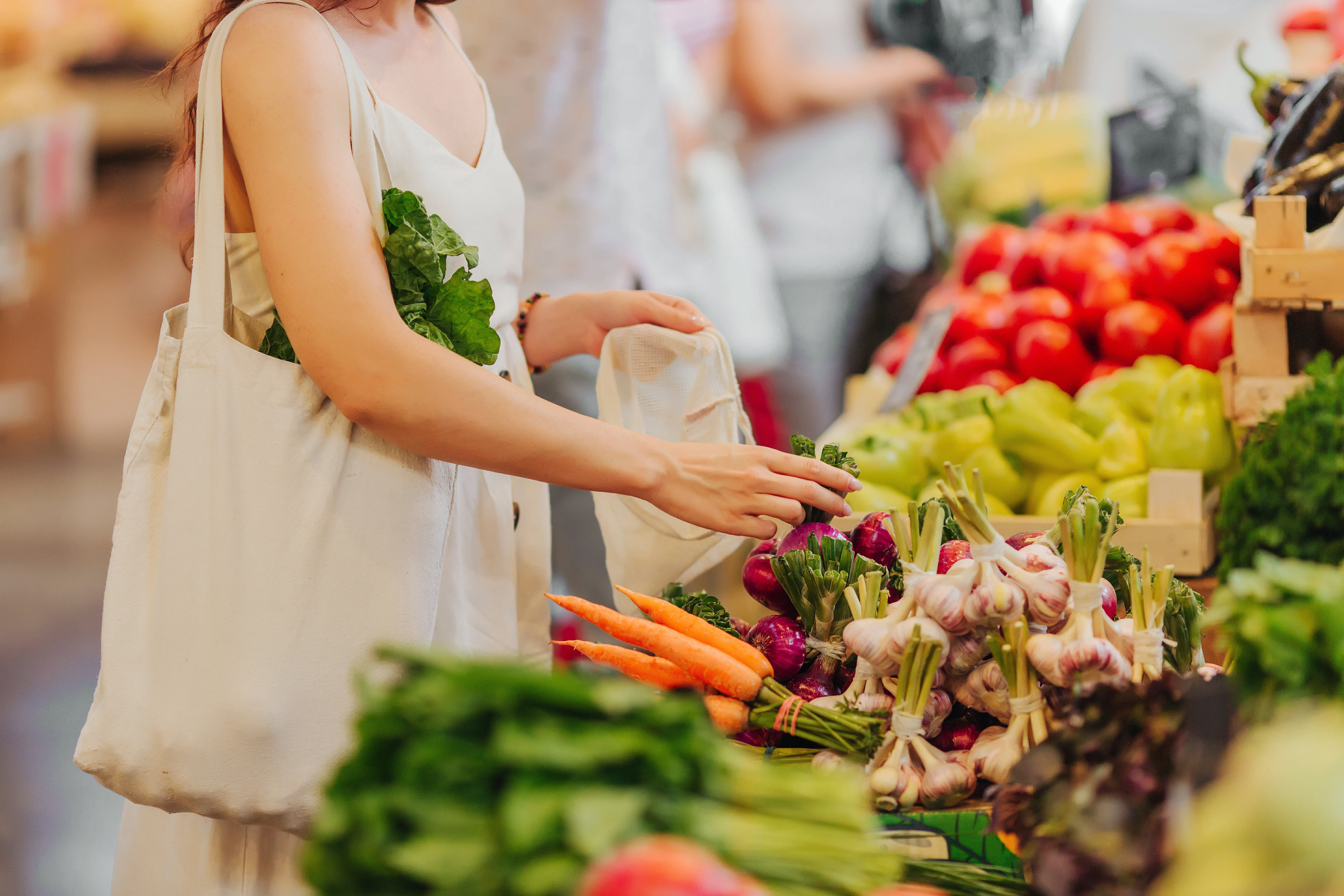 Female hands puts fruits and vegetables in cotton produce bag at food market. Reusable eco bag for shopping. Zero waste concept. Plastic-free alternatives.
