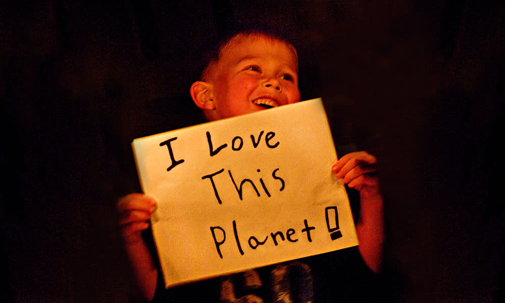 A young boy holding up a handmade sign reading I love this planet