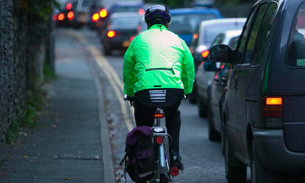 Cyclist commuting through a traffic jam, Ambleside, Cumbria, UK