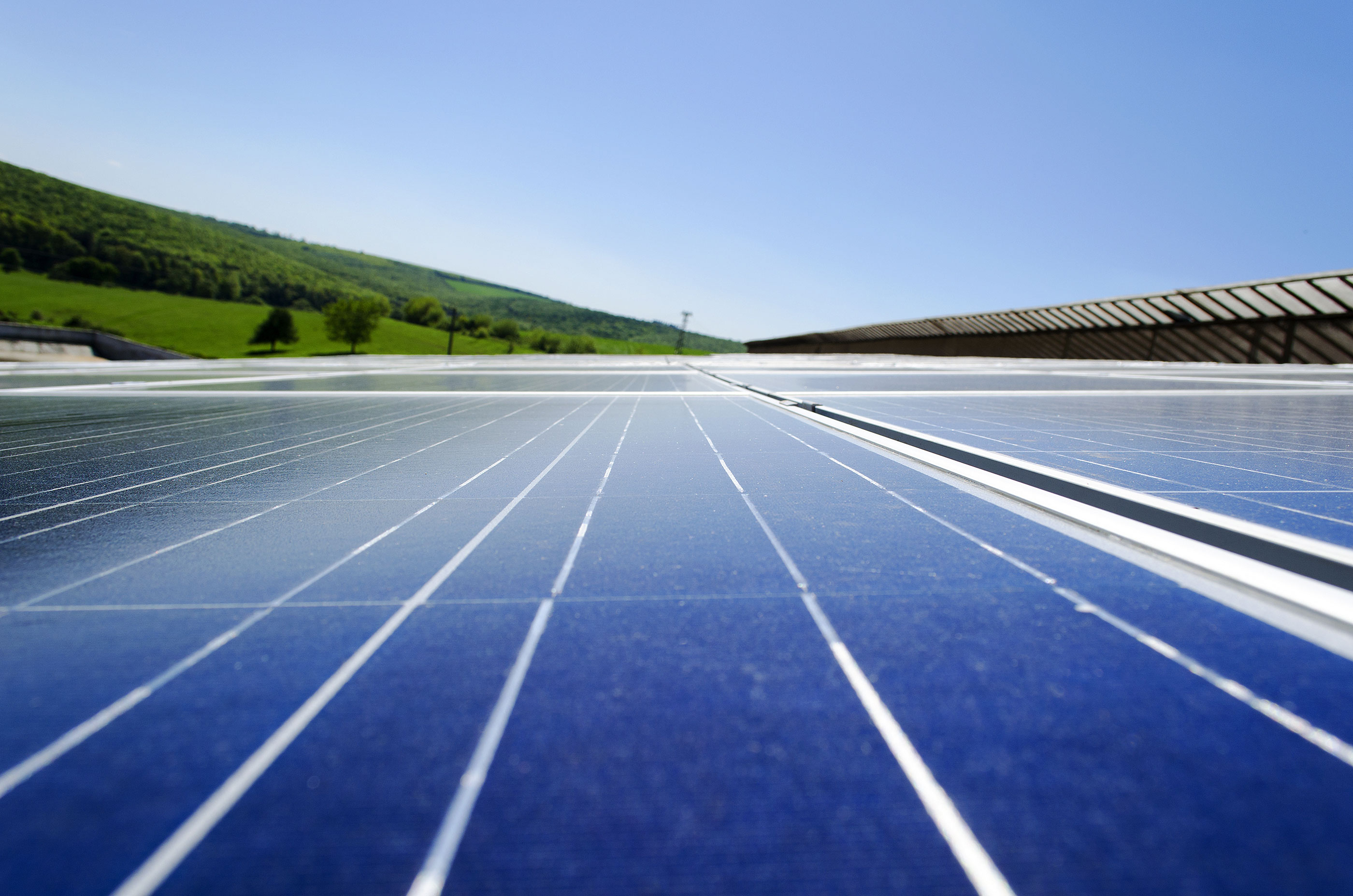 A stock image of solar panels in a rural setting. Green hills in background with renewable energy solar panels in the foreground.